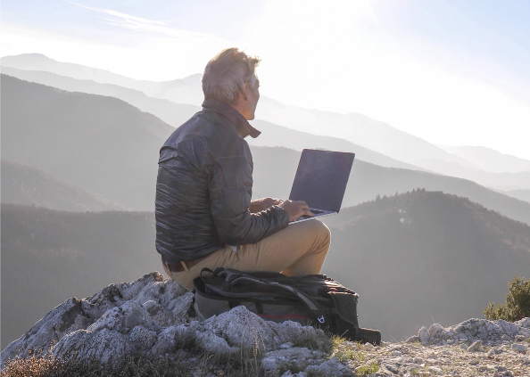 Man sitting on rock with laptop looking out at mountains